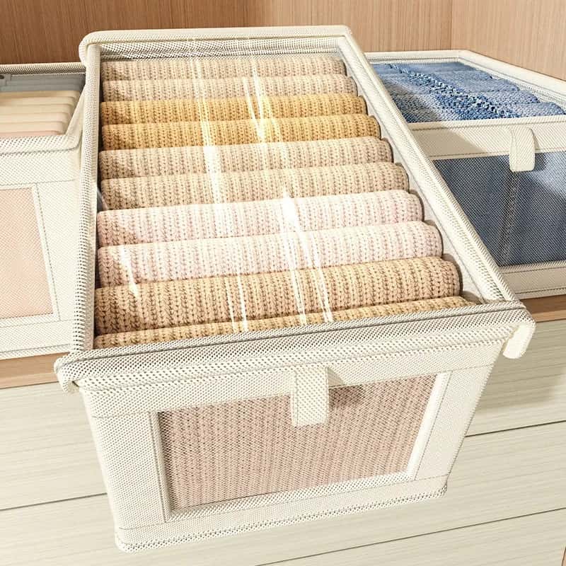Beige fabric storage box with a clear zippered top and mesh front window, neatly holding folded sweaters.