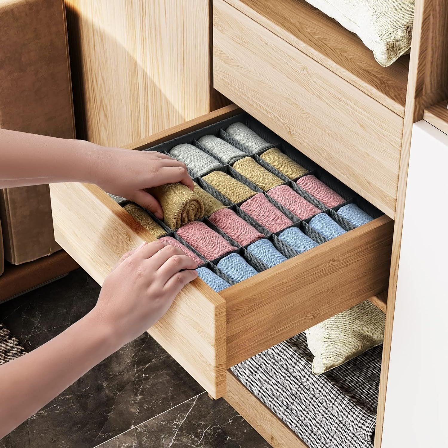 Hands arranging rolled colorful socks in a compartment organizer inside an open wooden drawer.
