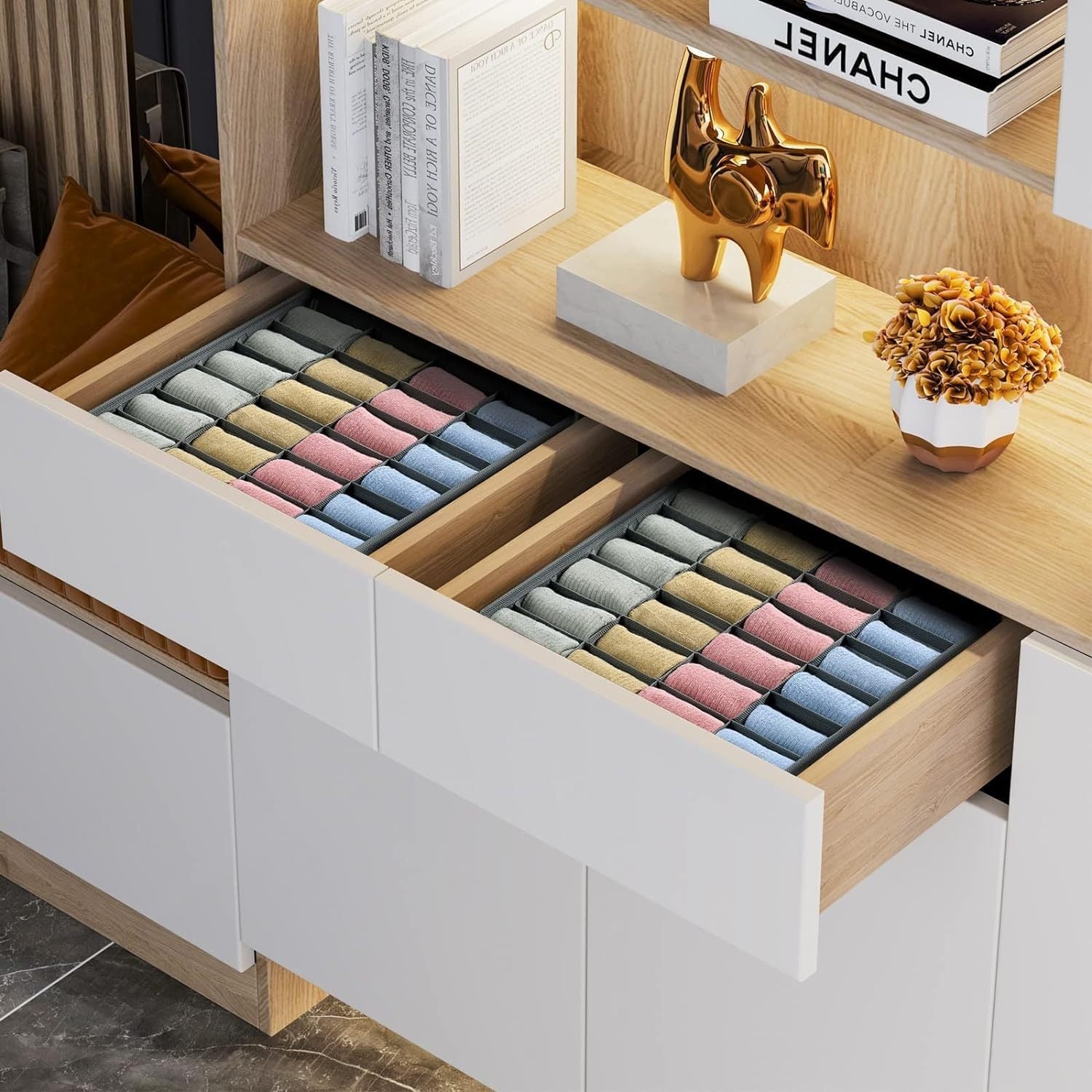 Two open cabinet drawers with compartment organizers holding neatly rolled colorful socks beneath a wooden display shelf.