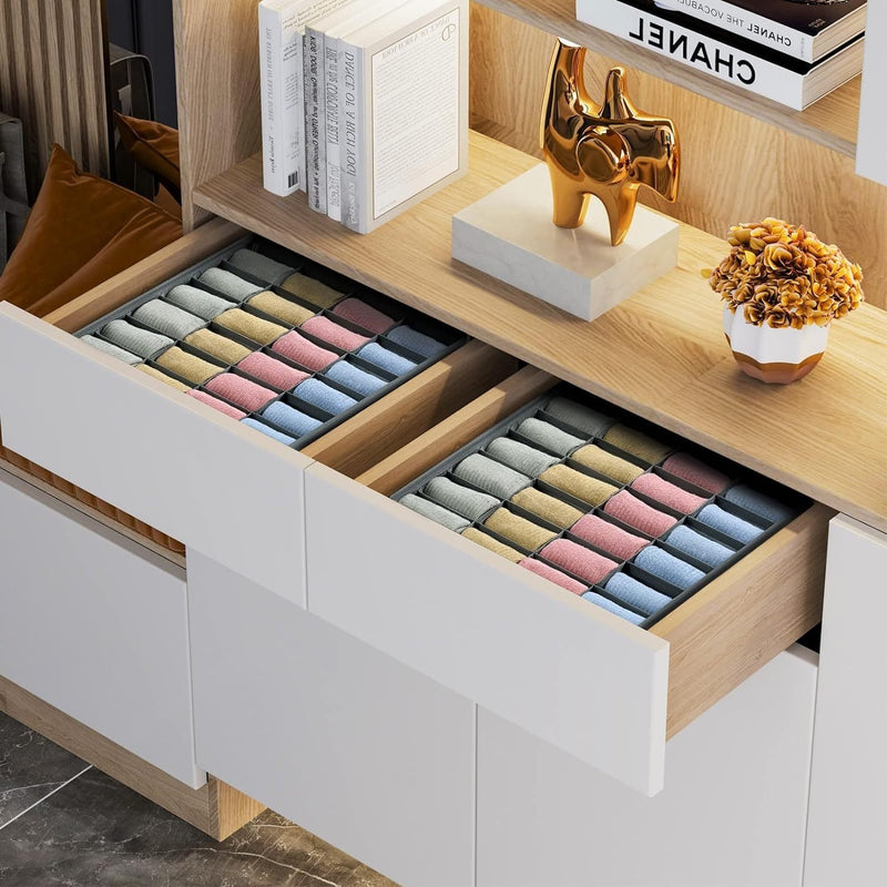Two open cabinet drawers with compartment organizers holding neatly rolled colorful socks beneath a wooden display shelf.